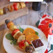 Text overlay: cadryskitchen.com. Thanksgiving-style vegan kebabs. Skewer on plate with persimmon slices and cranberry sauce.