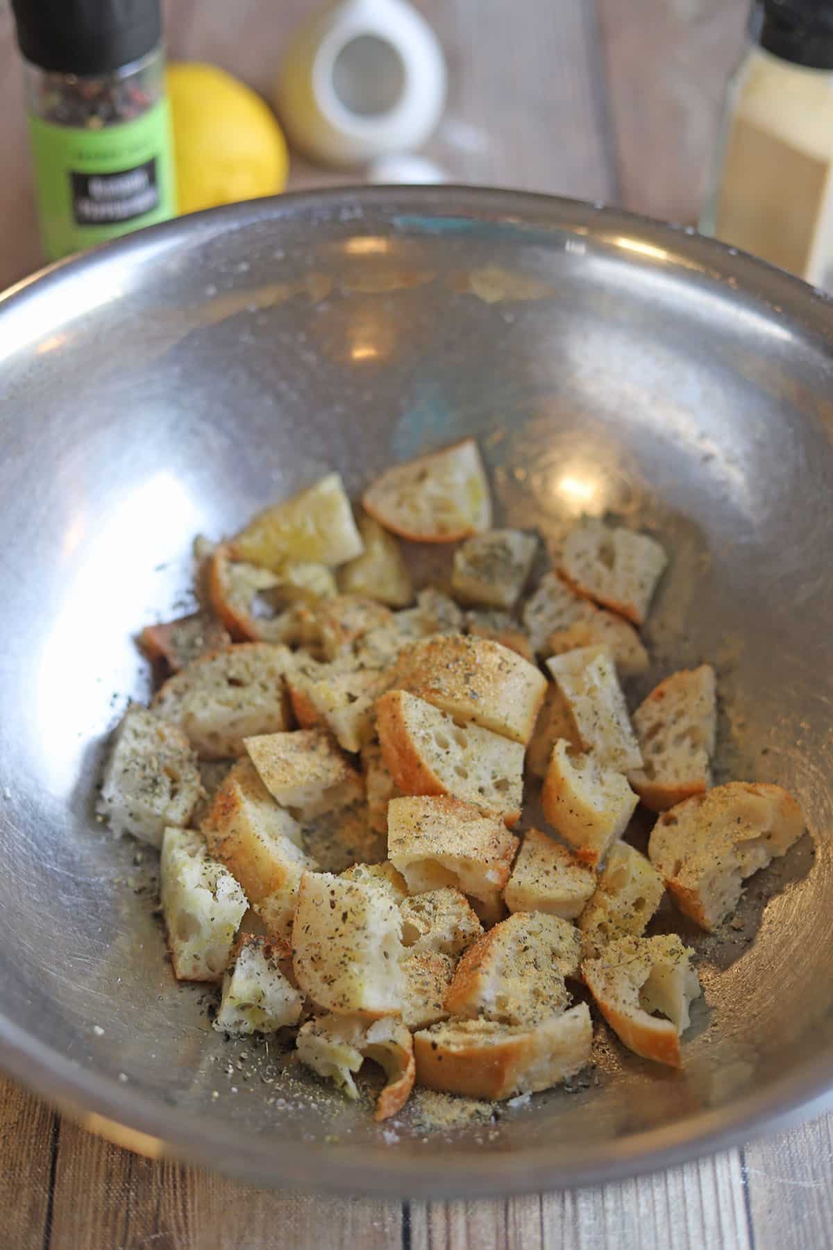 Bread cubes in mixing bowl with dried herbs and lemon juice.