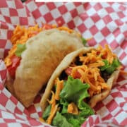 Text overlay: Vegan puffy tacos. Checkered basket with vegan puffy tacos, inspired by Tasty Tacos in Des Moines, Iowa.