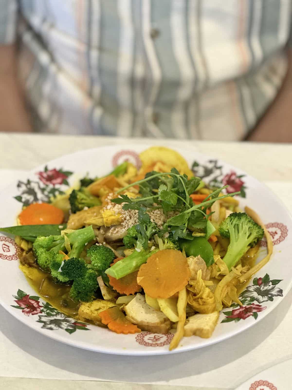 Tofu stir-fried with curry and vegetables on floral plate.