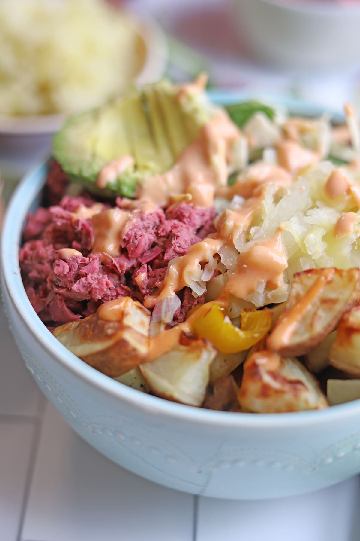 Close-up corned jackfruit and potatoes in blue bowl and smothered with dairy-free thousand island dressing.