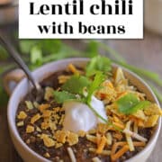Text overlay: cadryskitchen.com, lentil chili with beans. Hearty chili in bowl topped with crushed tortilla chips, sour cream, and cilantro.