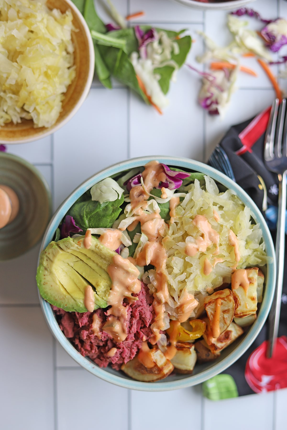 Overhead blue bowl with sauerkraut, corned jackfruit, avocado, vegan thousand island dressing, potatoes, and salad.