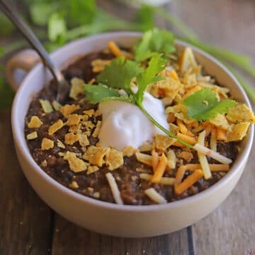 Lentil chili topped with non-dairy sour cream, shredded cheese, crushed chips, and cilantro.