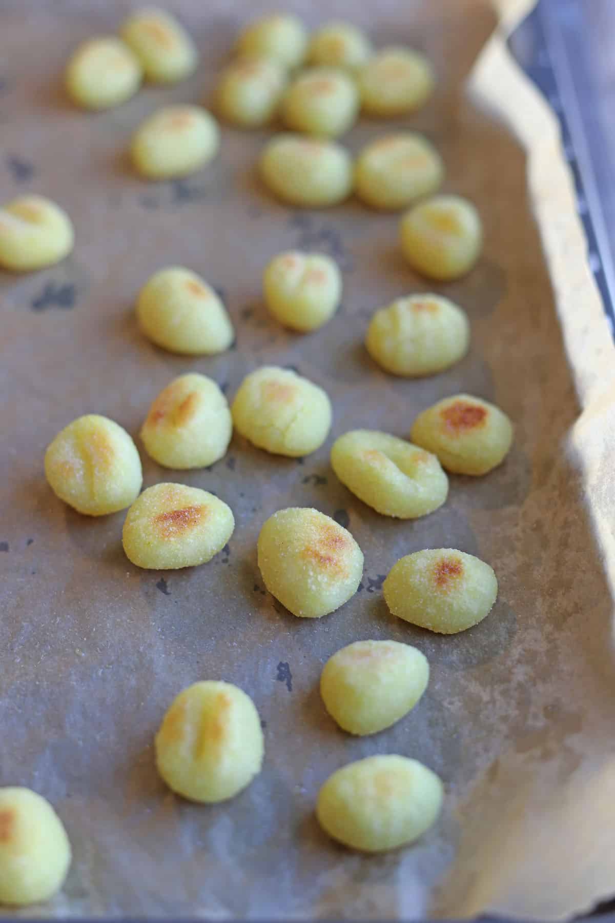 Browned gnocchi on parchment paper covered baking sheet.