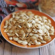 Crispy air fried pumpkin seeds on orange plate.