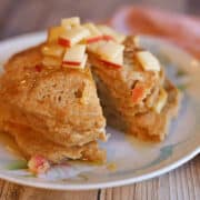 Stack of vegan apple cinnamon pancakes with fresh apple and maple syrup.