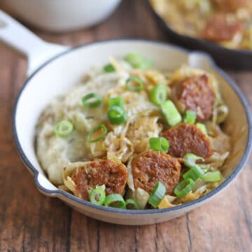 Vegan bratwurst with beer and sauerkraut on top of mashed potatoes in skillet.