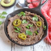 Vegan refried black beans in cast iron skillet, garnished with jalapenos and cilantro.