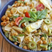 Bowtie pasta salad with fresh basil, artichoke hearts, cherry tomatoes, and Castelvetrano olives in bowl.