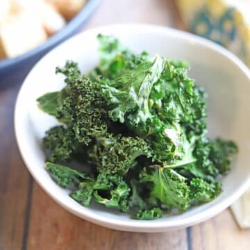 Crispy air fried kale chips in white bowl.