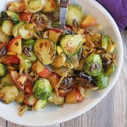 Roasted Brussels sprouts with apples, pistachios, and caramelized onions in serving dish with spoon.