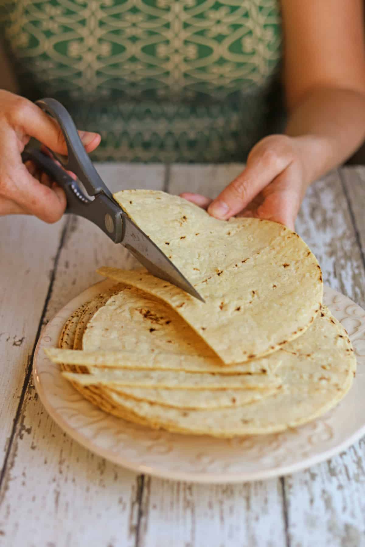 Kitchen shears being used to cut soft corn tortillas into strips.