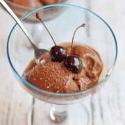 Chocolate banana nice cream in glass bowls garnished with maraschino cherry.