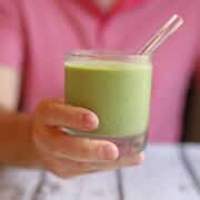 Hand holding green cashew kale smoothie with glass straw.