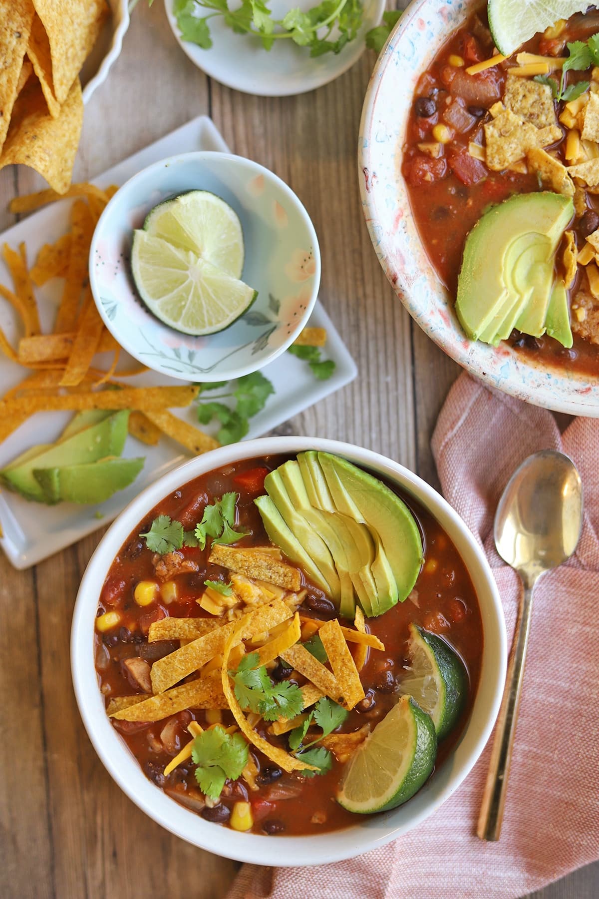Vegan tortilla soup garnished with avocado, limes, cilantro, and crispy corn tortilla strips.