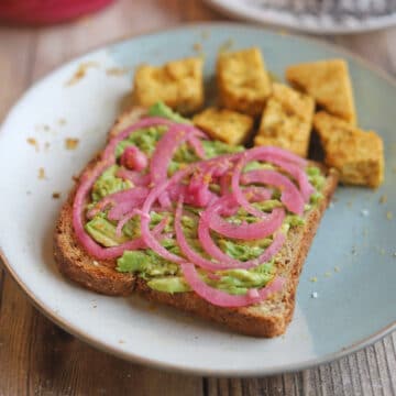 Avocado toast topped with hot pink pickled onions by nutritional yeast tofu.