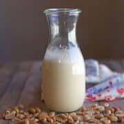 Glass bottle filled with homemade peanut milk, surrounded by roasted peanuts.