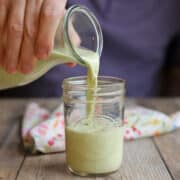 Homemade pistachio milk with light green color being poured from bottle into glass.