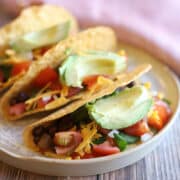 Black bean tacos in crunchy shells with avocado and shredded vegan cheese.
