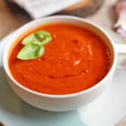 Creamy vegan tomato soup in bowl with drizzle of sun-dried tomato oil and fresh basil.