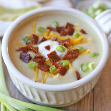 Vegan baked potato soup topped with seitan bacon, shredded cheddar style cheese, and green onions in bowl.