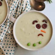 Vegan snowman soup frowning in bowl by spoons and napkin.