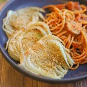 Slices of vegan parmesan coated fennel on blue plate with spaghetti and mushrooms.