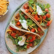 Vegan chicken tacos on platter by shredded non-dairy cheese.