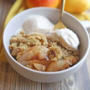Vegan pear crisp in bowl with oats and pistachios by dollops of non-dairy ice cream.