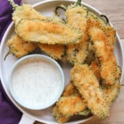 Fried vegan jalapeno poppers with dipping sauce on plate.