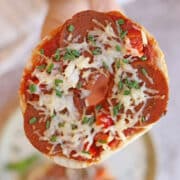 Hand holding air fried vegan pizza bagel with seitan pepperoni and non-dairy cheese.