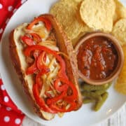 Vegan Philly cheesesteak with jackfruit, peppers, onions, and cashew cheese sauce on plate with tortilla chips & salsa.