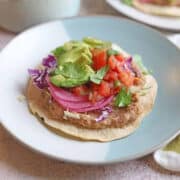 Air fried tostadas with refried beans, pickled onions, avocado, salsa, and cilantro on plate.