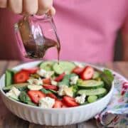 Balsamic vinaigrette being poured onto spinach salad with strawberries, cucumbers, and vegan feta.