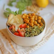 Bowl with pesto rice, roasted chickpeas, cherry tomatoes, and an artichoke heart.