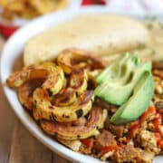 Roasted delicata squash by tofu scramble, avocado slices, and corn tortillas on platter.