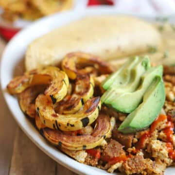 Roasted delicata squash by tofu scramble, avocado slices, and corn tortillas on platter.