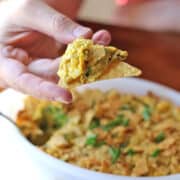 Vegan spinach and artichoke dip on tortilla chip over casserole dish.