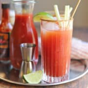 Vegan Bloody Mary on tray by mix in jar, shot of vodka, lime wedge, and hot sauce.