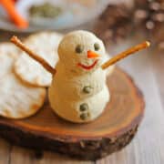 Vegan snowman cheeseball made with tofu, capers, carrot, bell pepper, and pretzel sticks.