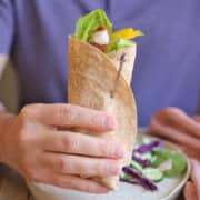 Hand holding vegan chicken wrap with tahini drizzle.