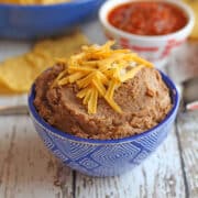 Vegan refried beans in blue bowl topped with shredded non-dairy cheese.