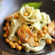 Pesto pasta with roasted chickpeas and browned artichoke hearts in bowl.