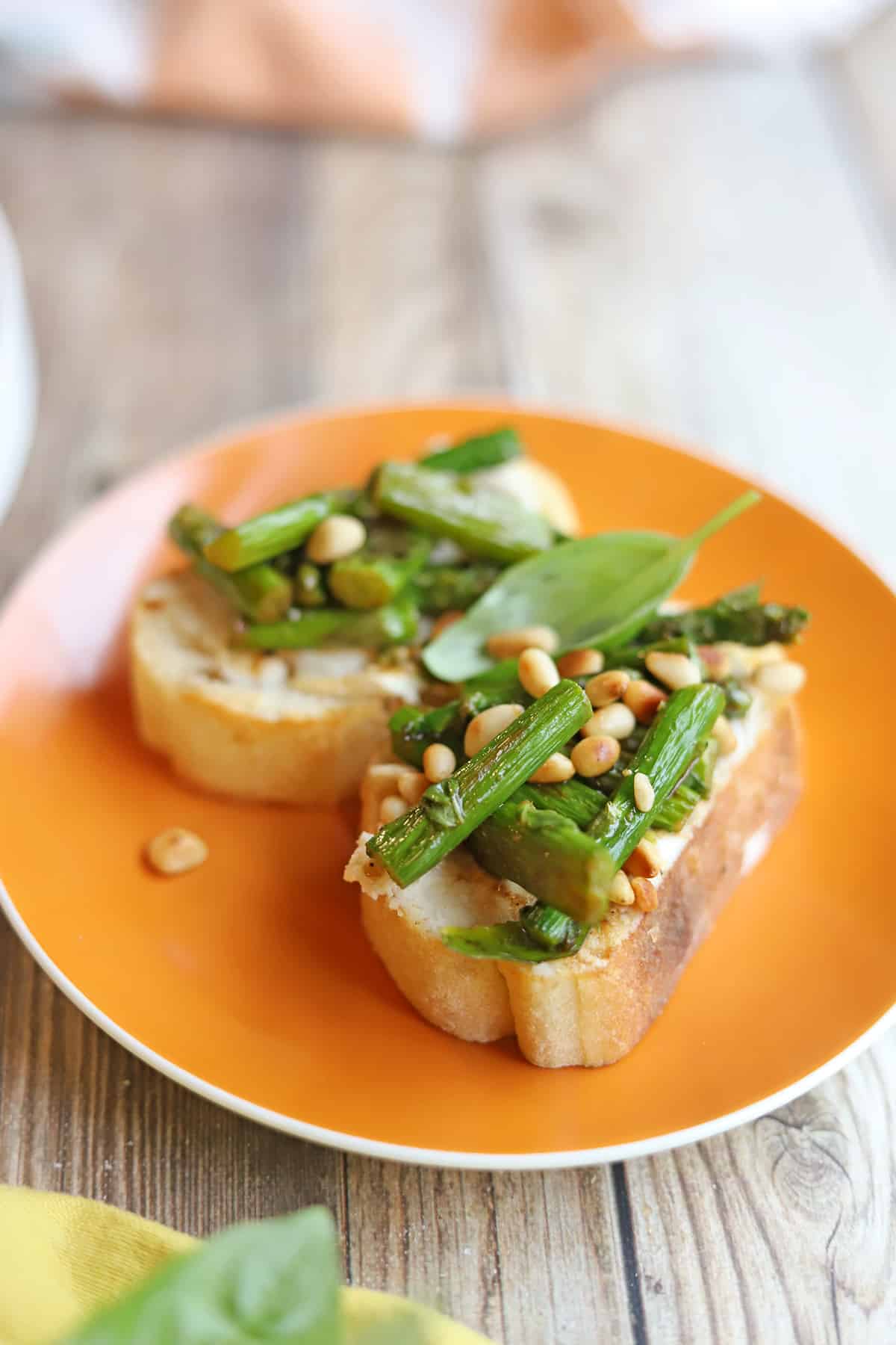 Roasted asparagus bruschetta on orange plate.