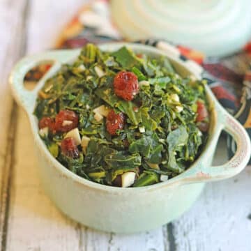 Garlicky collard greens dotted with dried cranberries in teal dish.