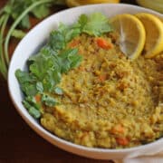 Vegan kitchari in bowl topped with cilantro and lemon wedges.