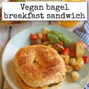 Text overlay: cadryskitchen.com, vegan bagel breakfast sandwich. Bagel breakfast sandwich on plate with potato & pepper hash.