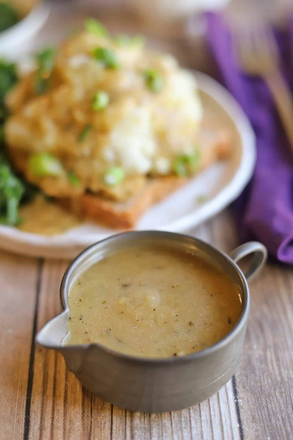 Vegan turkey gravy in front of hot open faced sandwich.