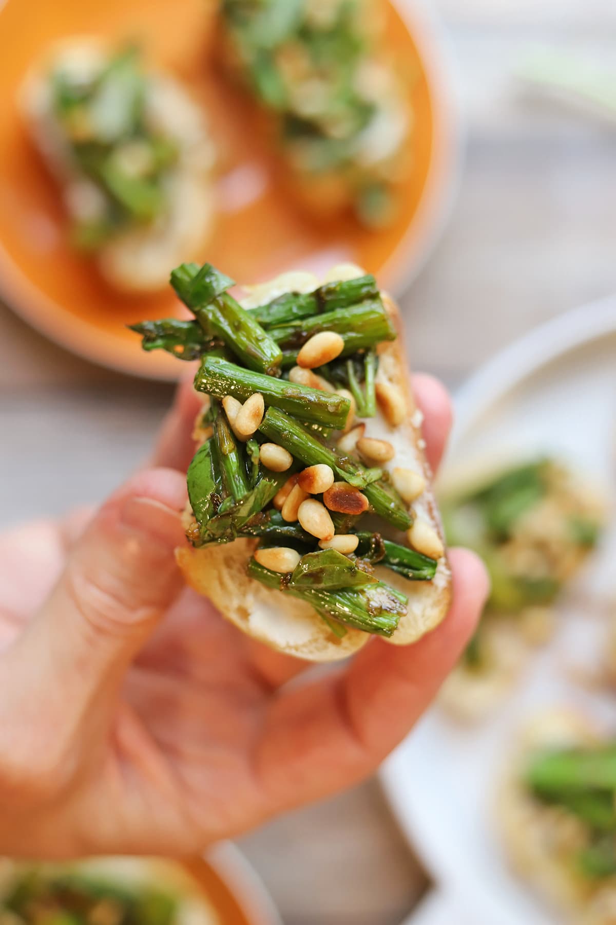 Hand holding roasted asparagus & pine nuts canapes.